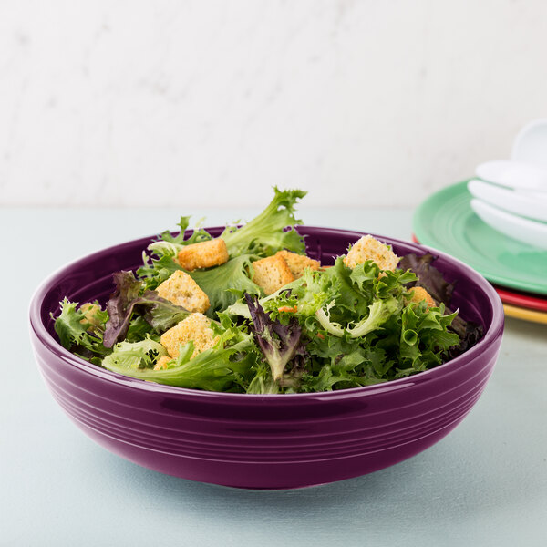 A Fiesta Mulberry china serving bowl filled with salad on a table.