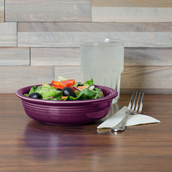 A purple Fiesta china bowl filled with salad on a table.