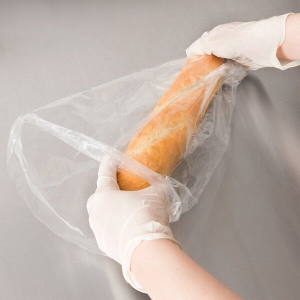 A person in gloves holding a loaf of bread in a plastic bread bag.