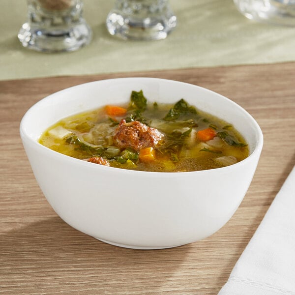 An Acopa Nova cream white stoneware bowl filled with soup containing meat and vegetables.