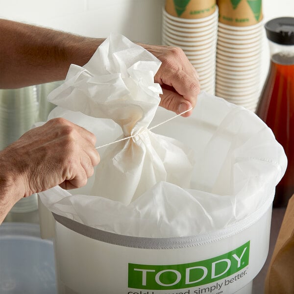 A person using a Toddy commercial cold brew filter to pull a string out of a trash can.