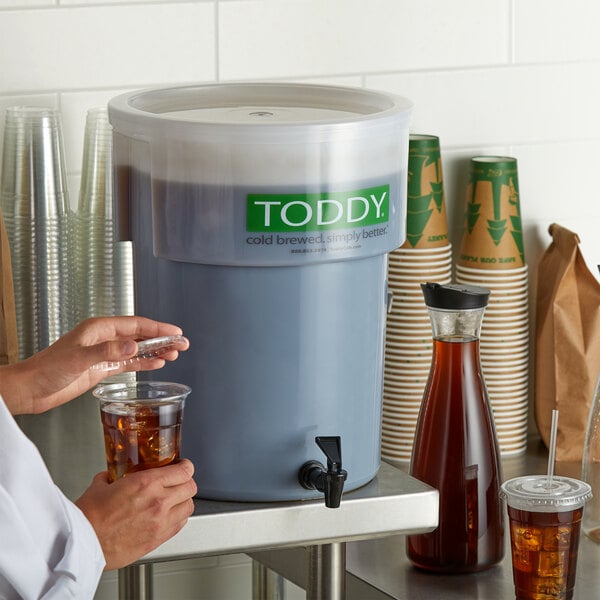 A woman using a Toddy cold brew system to pour coffee into a plastic cup with ice.