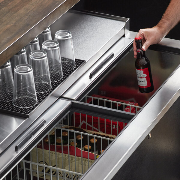 A hand holding a bottle of beer in a Beverage-Air deep well bottle cooler on a bar counter.