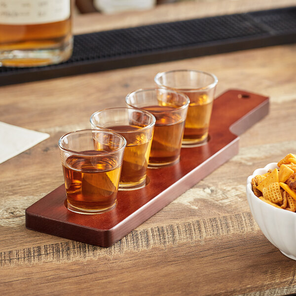 An Acopa mahogany wood flight paddle holding three tasting glasses filled with brown liquid.