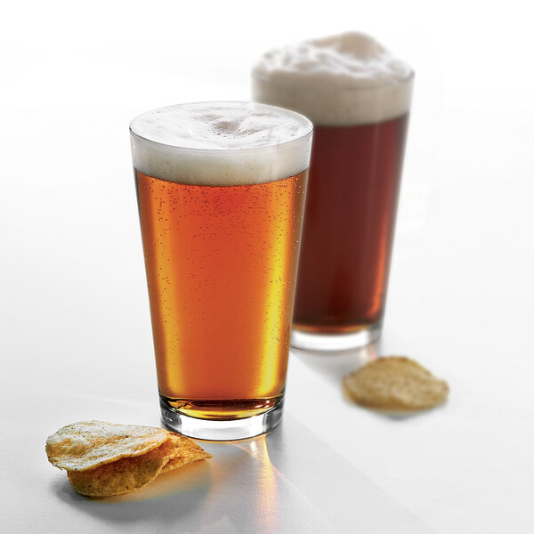 Two Arcoroc heavy sham mixing glasses of beer with foam and potato chips on a white surface.