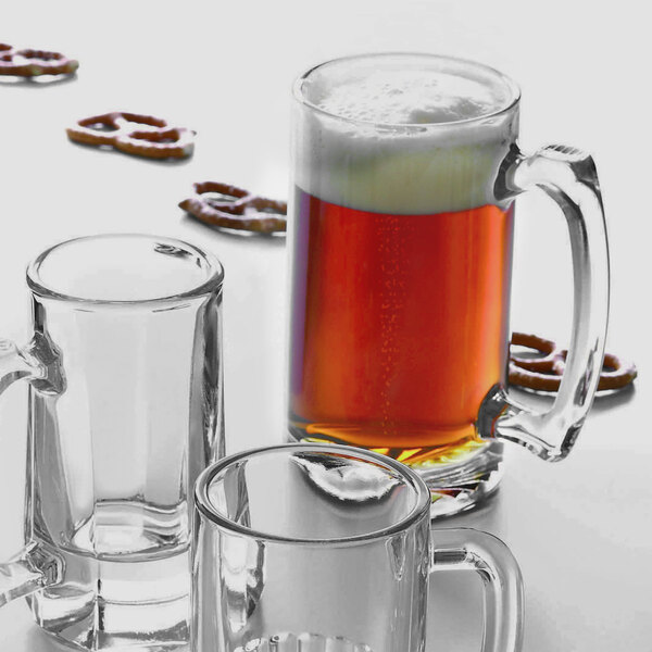 An Arcoroc glass mug filled with beer on a table with pretzels.