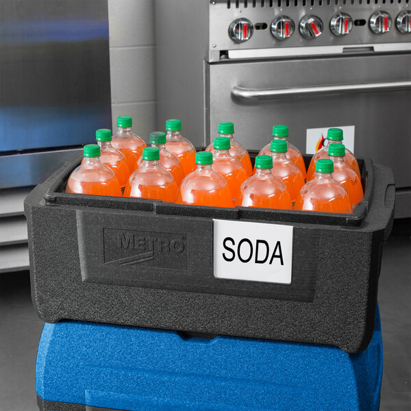 A black Metro Mightylite BigBoy food pan carrier with a blue lid full of orange soda bottles.