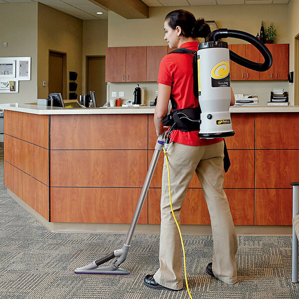 A woman using a ProTeam backpack vacuum cleaner to vacuum a room.