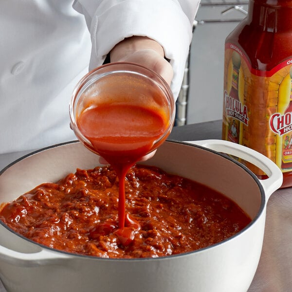 A person pouring Cholula hot sauce into a pot of food.