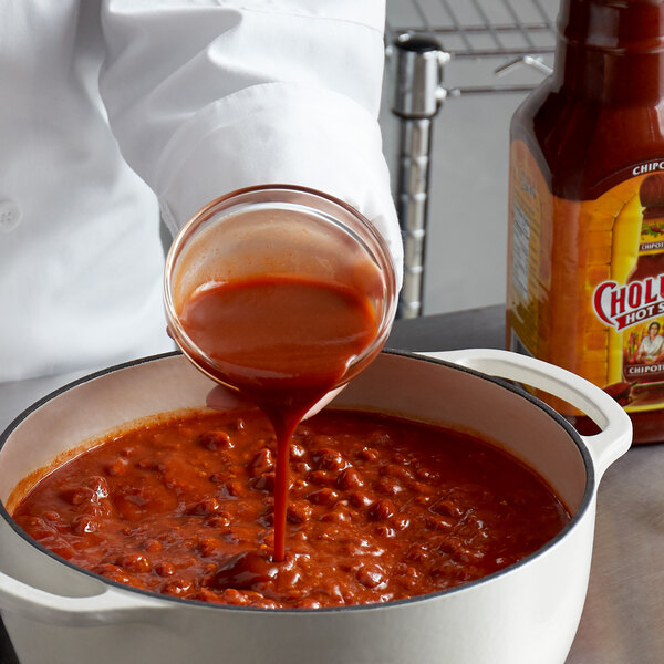 A person pouring Cholula Chipotle hot sauce into a pot of chili.