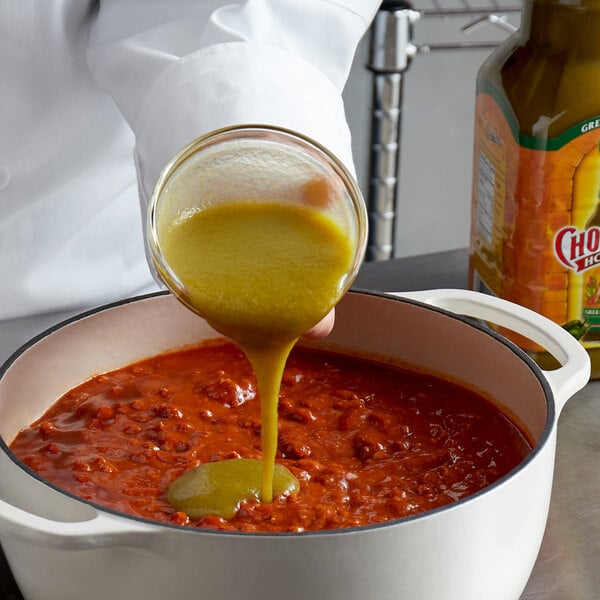 A person pouring green Cholula hot sauce into a pot of sauce.