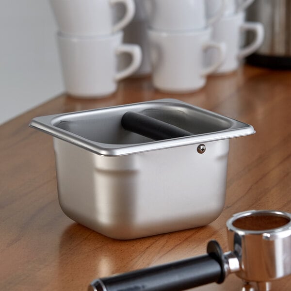 A stainless steel Vollrath knock box on a counter.