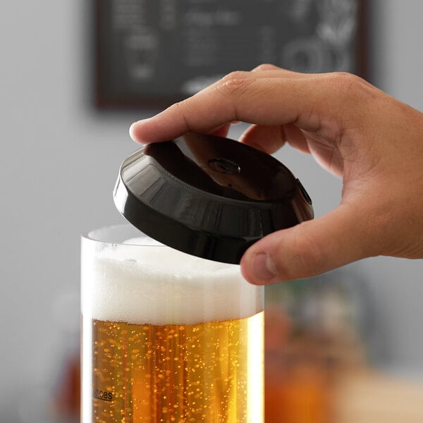 A hand using a black Beer Tubes lid to pour a glass of beer.