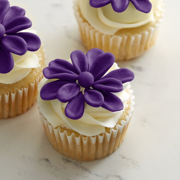 Three cupcakes with Satin Ice ChocoPan purple flowers on top.