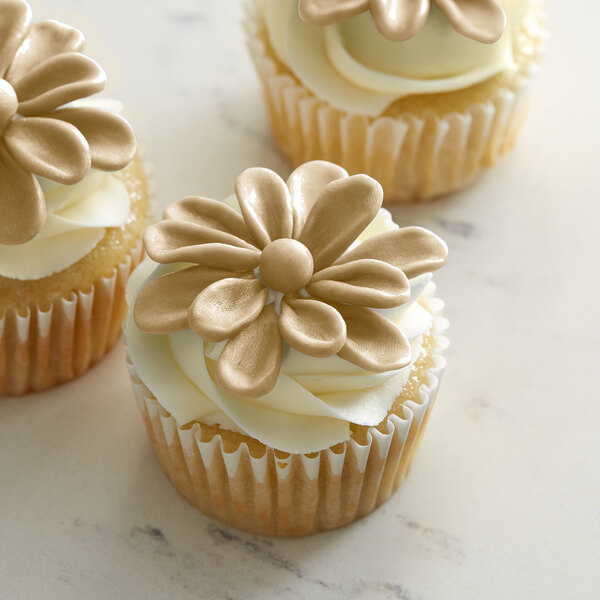 A group of Satin Ice ChocoPan Warm Sand cupcakes with white frosting and gold flowers.