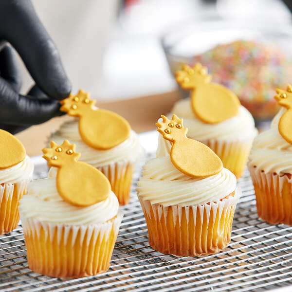 A person holding a pineapple cookie on top of cupcakes with gold shimmer fondant decorations.