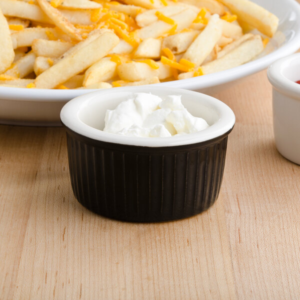 A bowl of french fries with cheese and sour cream in a fluted Tuxton ramekin.