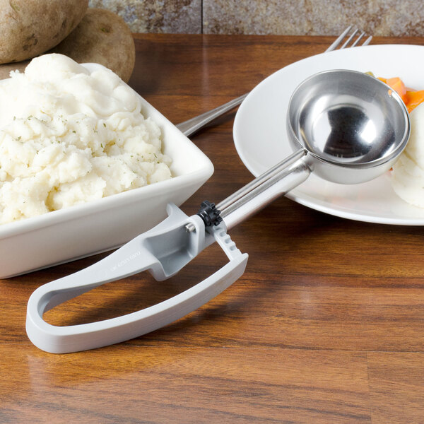 A bowl of mashed potatoes with a Vollrath gray extended length scoop on a table.