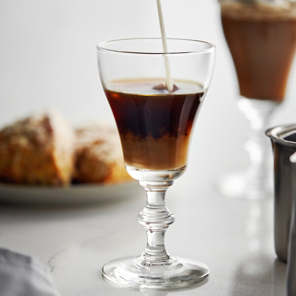 A Libbey Irish coffee glass filled with a brown liquid and a spoon pouring milk into it.