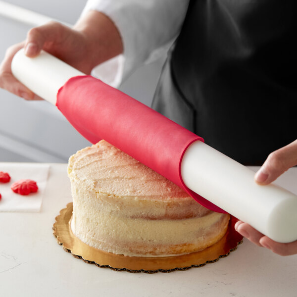 A person using a pink Satin Ice ChocoPan roll to cover a cake.