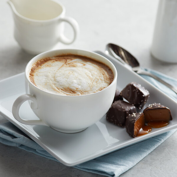 A white cup of UPOURIA Salted Chocolate Caramel Cappuccino on a white saucer with chocolates.