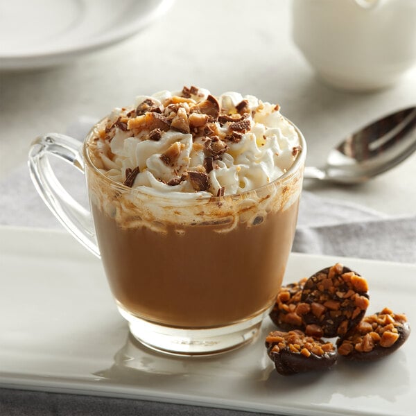 A glass mug of UPOURIA English toffee cappuccino with whipped cream and nuts.