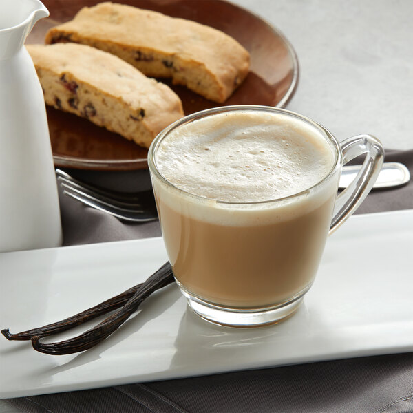 A glass mug of UPOURIA French vanilla cappuccino with a vanilla bean on the side.