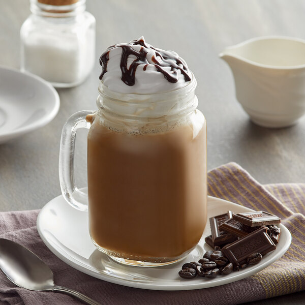 A glass mug of UPOURIA Mocha Latte with whipped cream and chocolate bars on a plate.