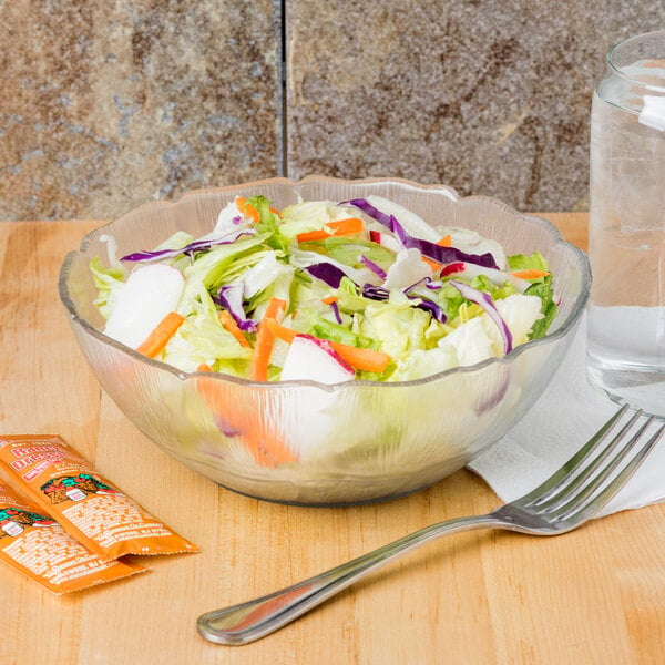 A Carlisle Petal Mist clear polycarbonate bowl filled with salad with a fork.