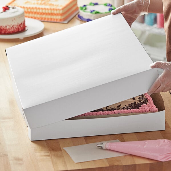 A person opening a white Baker's Mark full sheet cake box.