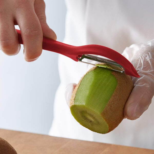 A hand using a Victorinox red straight vegetable peeler to peel a kiwi.