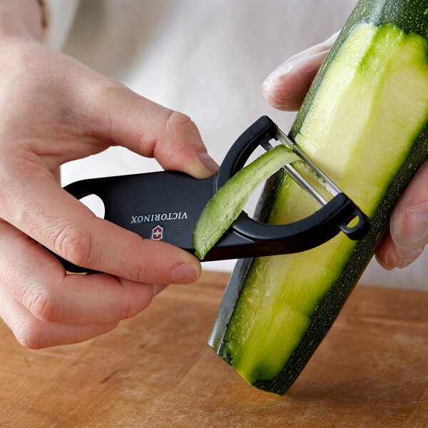 A person using a Victorinox black off-set "Y" vegetable peeler to peel a cucumber.