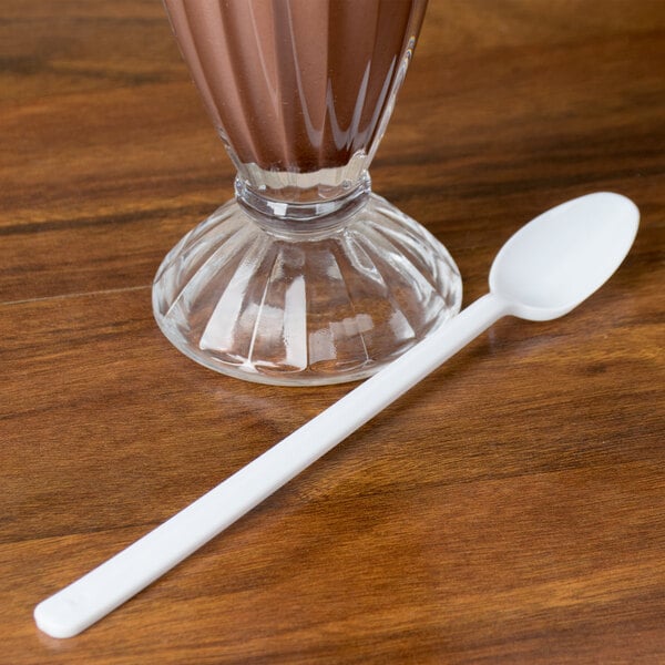 A clear glass of chocolate milkshake with a white Dart plastic spoon.