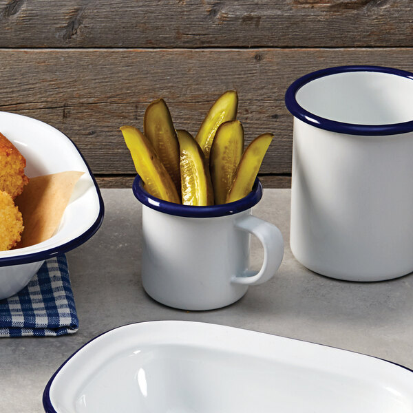 An American Metalcraft white enamel mug with a blue rim filled with pickles.