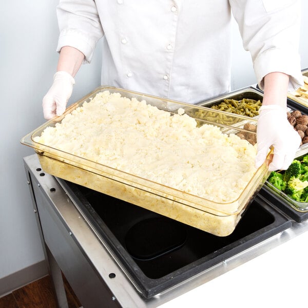A person in a white chef's uniform holding a Cambro amber plastic food pan full of food.
