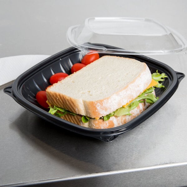A sandwich in a Dart black plastic bowl with tomatoes and lettuce.