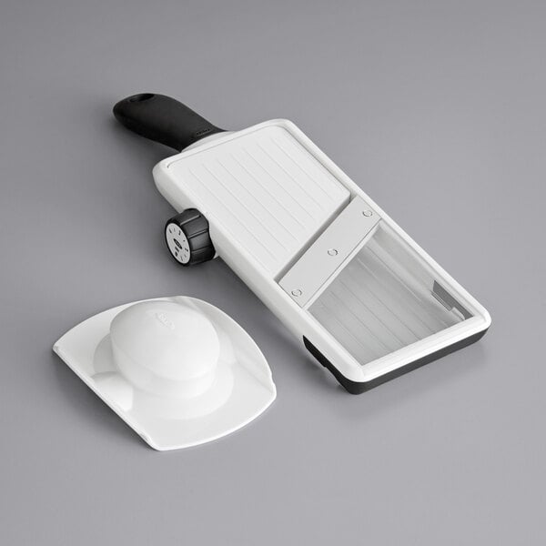 An OXO white and black hand-held mandoline slicer with a wheel.