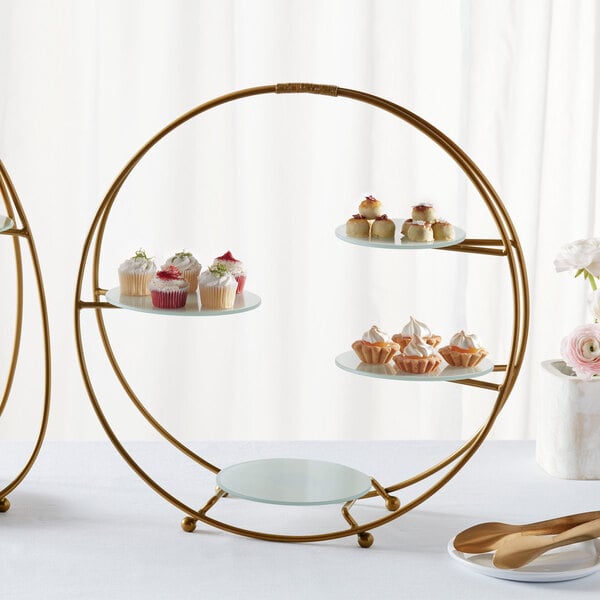 An American Metalcraft gold round stand with frosted glass plates holding cupcakes on a table.