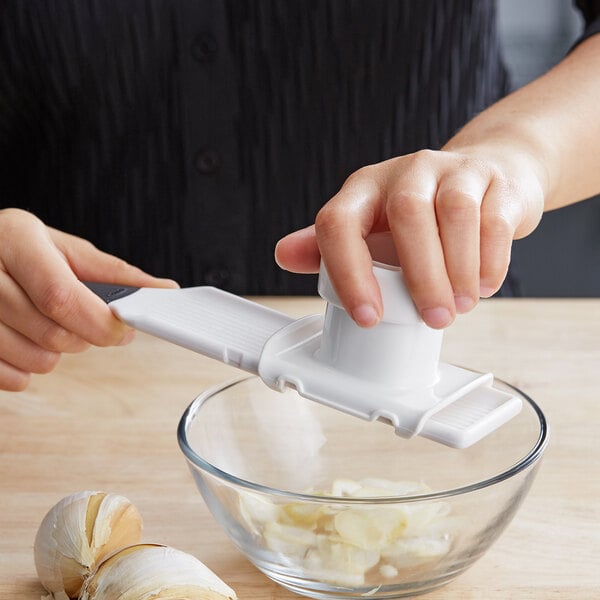 A hand using an OXO Good Grips garlic slicer to slice garlic.