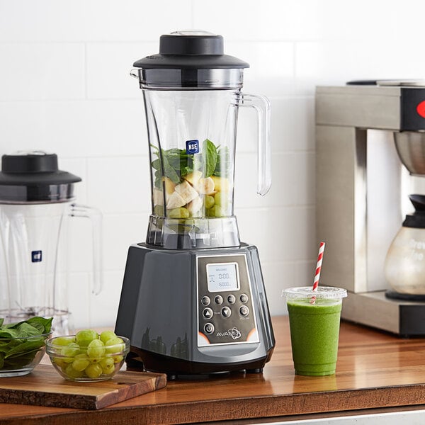A AvaMix commercial blender filled with green juice, grapes, and spinach on a counter.