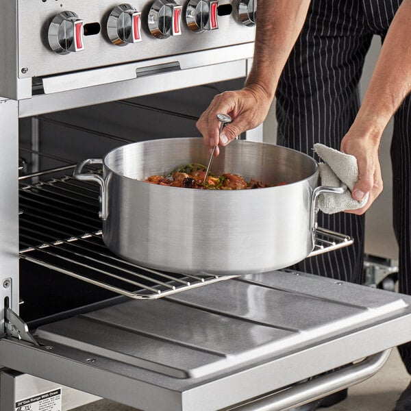 A person cooking food in a Choice Heavy-Duty Aluminum Brazier on a table in a professional kitchen.