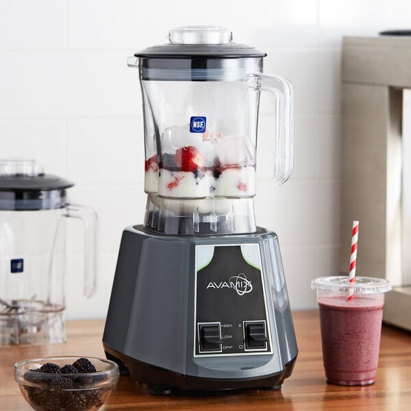 An AvaMix commercial blender with ice cubes, strawberries, and blackberries in a Tritan container.