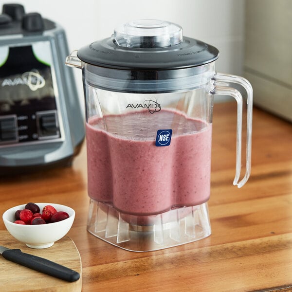A black AvaMix blender with pink smoothie in it on a wood surface.