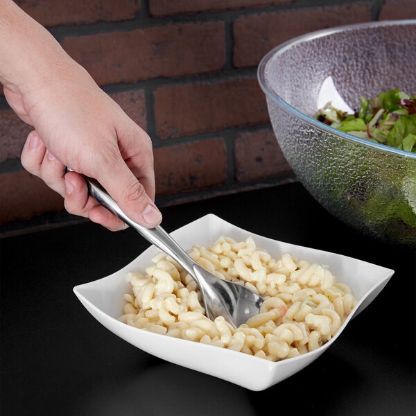 A hand using a Sabert silver plastic serving spoon in a bowl of macaroni and cheese.