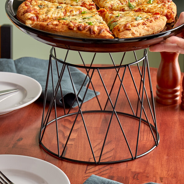 An American Metalcraft black metal wire frame pizza stand holding a plate of pizza on a table.