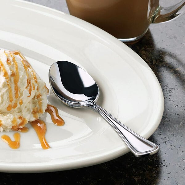 A white plate with a Libbey McIntosh stainless steel teaspoon and a scoop of ice cream.
