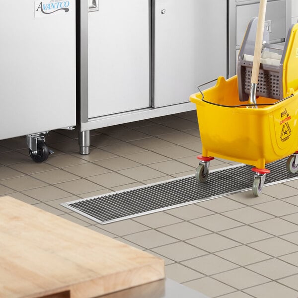 A yellow mop and bucket sitting on a white floor near a Regency stainless steel floor trough.