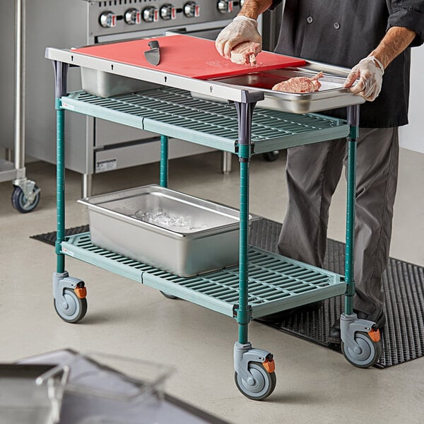 A man using a Metro Prepmate Butcher Prep Cart to hold a tray of meat.