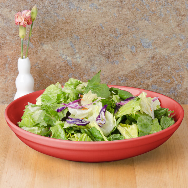 A CAC red salad bowl filled with salad on a wooden table.