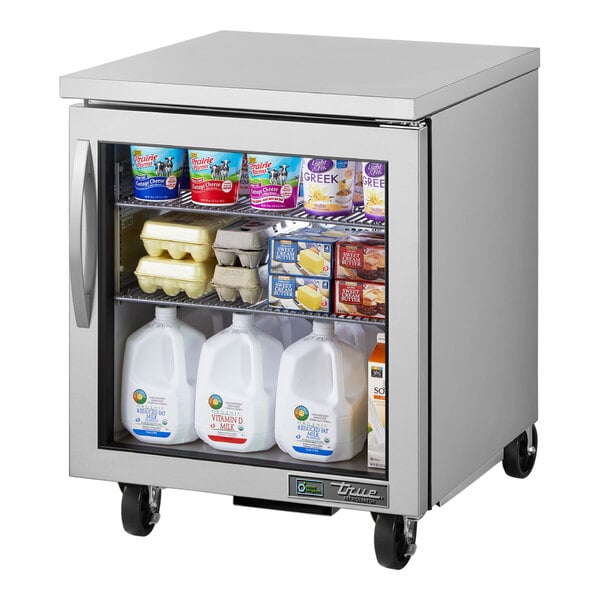 A True undercounter refrigerator with a glass door filled with dairy products including a white plastic container and a jug of milk.